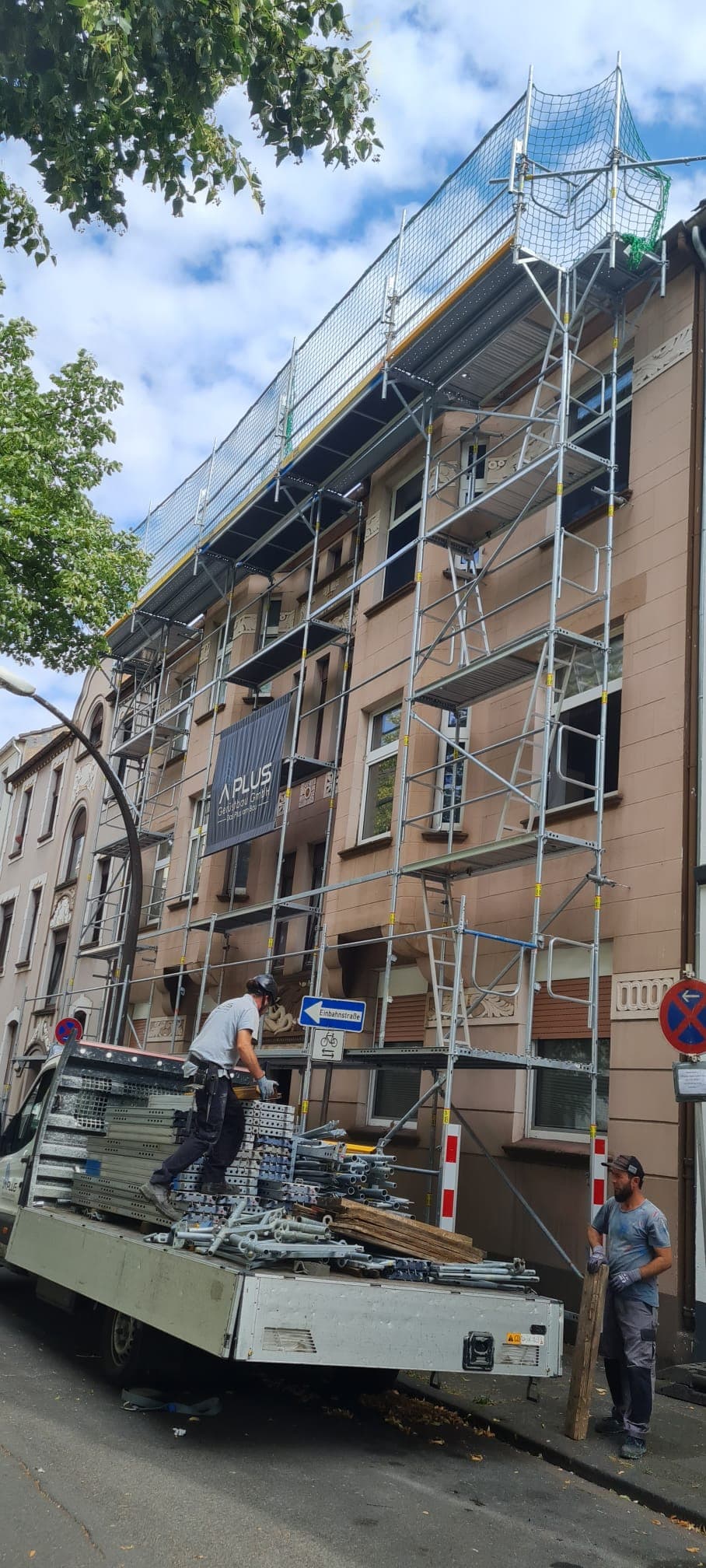 Gerüstbauer entladen Material vom Firmen-Lkw vor einer eingerüsteten Altbaufassade