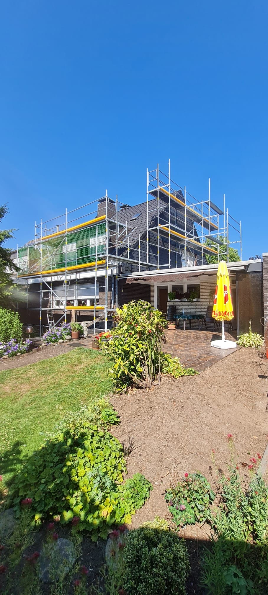 Gerüst mit Dachfangschutz und grünem Schutznetz an einem Wohnhaus mit Steildach